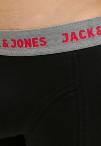 Schwarze Unterwäsche mit einem grauen elastischen Bund, auf dem "JACK & JONES" in roter Schrift steht. Glatte Textur mit einem körpernahen Design und Nahtdetails.