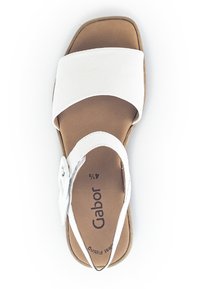 Hvide sandaler med brede, flade stropper og en sølvaccent. Blødt, glat materiale og en polstret brun indersål. Firkantet tå og åben bagside design.