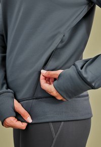 Hallide halli sportlik pullover, millel on küljes lukk tasku, pehme tekstuur, vormistatud disain ja varrukates pöidlahaugid.