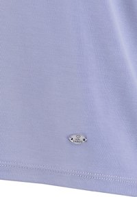 Lichtpaars stof met fijne stiksels en een klein ovaal zilveren label gegraveerd met een hart en de tekst "KEY LARGO".