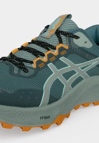 Γκρι και πορτοκαλί παπούτσι τρεξίματος ASICS με μαύρα κορδόνια, διχτυωτό επάνω μέρος, λογότυπο στο πλάι και υφασμένη πορτοκαλί σόλα για πρόσφυση και απορρόφηση κραδασμών.