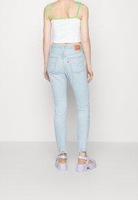 Light blue high-waisted jeans with a close fit, frayed hem, and back pockets. Paired with a white crop top with green accents and lavender sandals.