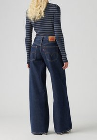 Höga, vida denimjeans i mörkblått med orange sömmar och en märkesläderpatch på baksidan. Mjuk, texturerad tyg.