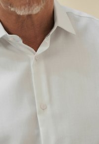 Weißes strukturiertes Hemd mit einem Knopfverschluss-Design, einem subtilen gemusterten Akzent unter dem Kragen und durchsichtigen Knöpfen.