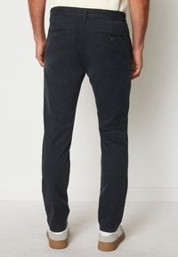 Chinos blu scuro con un design elegante a gamba dritta, due tasche posteriori con bottoni e una trama di tessuto liscia. Indossati con sneakers chiare.