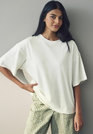 Witte oversized t-shirt gemaakt van zachte katoen, met korte mouwen en een ronde hals, gecombineerd met groene geblokte cargobroek.