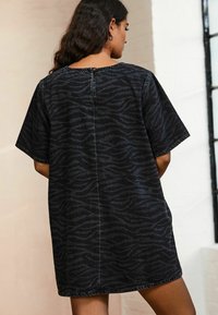Robe en denim noir avec un motif subtil de rayures zébrées, manches courtes, coupe loose, et un détail de bouton à l'arrière.