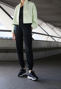 Mintgrön jacka med dragkedja, svarta tajta byxor med Nike-logotyp och svarta sneakers med vita sulor. Mjukt tyg med avslappnad passform.