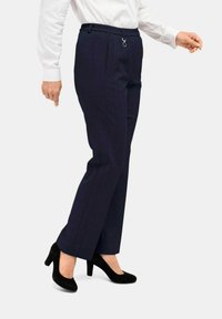 Marineblauwe broeken met een subtiele ruitpatroon, voorzien van een geplooide tailleband en een buitenzak, gecombineerd met zwarte suède hakken.