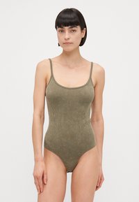 Maillot de bain une pièce côtelé vert olive avec des bretelles fines et un décolleté dégagé, offrant une coupe ajustée et une texture lisse.
