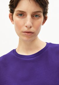 Paarse katoenen t-shirt met een klassieke ronde halslijn. Close-up toont de gladde textuur en het eenvoudige ontwerp zonder versieringen.