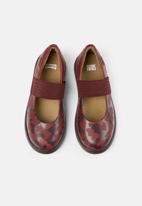 Scarpe rosse di pelle con motivi a cuore, punta arrotondata e una fascia elastica sopra il dorso del piede, con una fodera interna color beige e suola robusta.