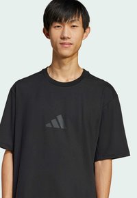 Black t-shirt crafted from soft fabric, featuring short sleeves, a round neckline, and a subtle dark graphic logo on the chest.