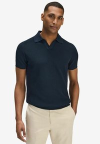 Navy short-sleeve polo shirt with a textured design and a V-neck collar, paired with light beige trousers, showcasing a modern fit.