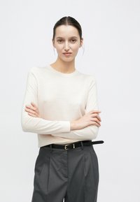 Top rosa chiaro a maniche lunghe con scollo rotondo, abbinato a pantaloni grigi a vita alta e una cintura nera sottile con fibbia dorata.