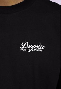 Schwarzes Baumwoll-T-Shirt mit weißem, geschwungenem und fettem Text, der "Dropsize" und "FROM THE ARCHIVES" auf der linken Brustseite zeigt.