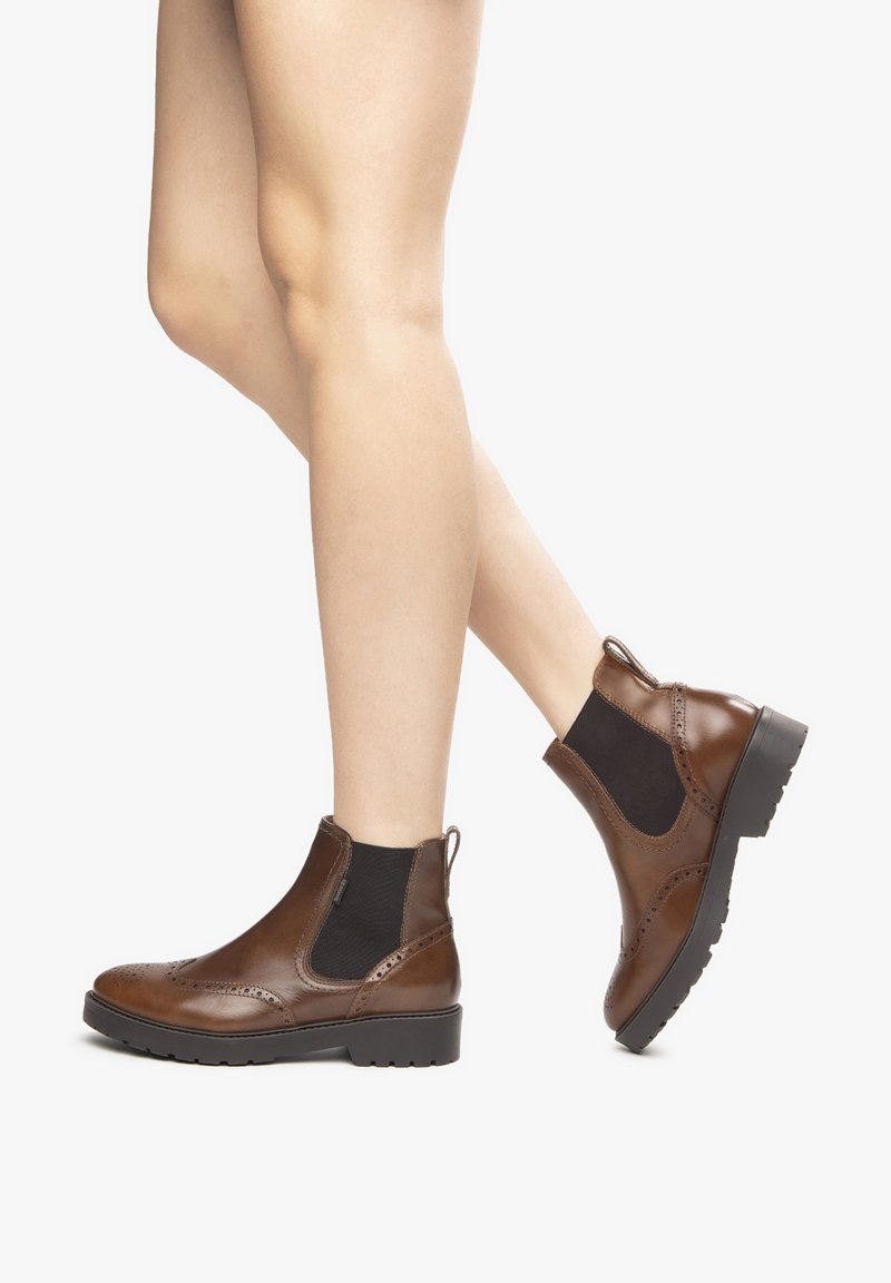 Bottines en cuir marron à panneaux élastiques sur les côtés, avec des détails perforés décoratifs et une semelle épaisse noire.