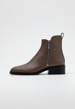 Botte cheville en cuir marron avec fermeture éclair latérale, talon noir empilé bas et languette à l'arrière, présentée sur un fond blanc uni.