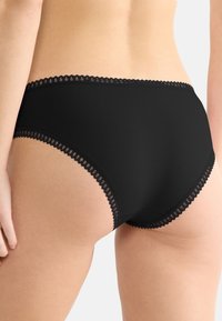 Svart högmidjad trosa med spetsdetaljer längs kanterna, som har ett slätt material med en svag lyster och en figurnära design.