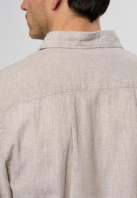 Camisa de rayas beige claro con cuello clásico, que presenta una textura sutil y un detalle de yugo en la parte trasera, además de acentos cosidos en toda la prenda.