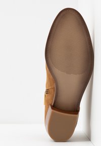 Brown suede shoe with a smooth rubber sole, featuring a tapered heel and textured detailing on the bottom for grip.