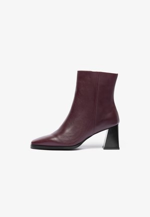 Bottine en cuir bordeaux à bout pointu et à talon géométrique noir épais ; texture lisse avec des détails de couture minimaux.