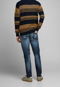 Stickad tröja med horisontella marinblå och senapsfärgade ränder, kombinerad med smala blå jeans och ljusbeige sneakers. Tydlig tygstruktur synlig.