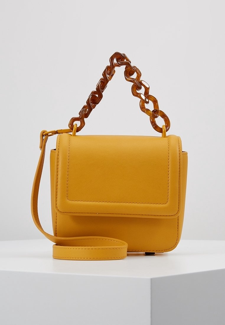 Sac à main en cuir jaune de forme rectangulaire, avec un rabat à l'avant, une bandoulière amovible et une anse épaisse en chaîne transparente.
