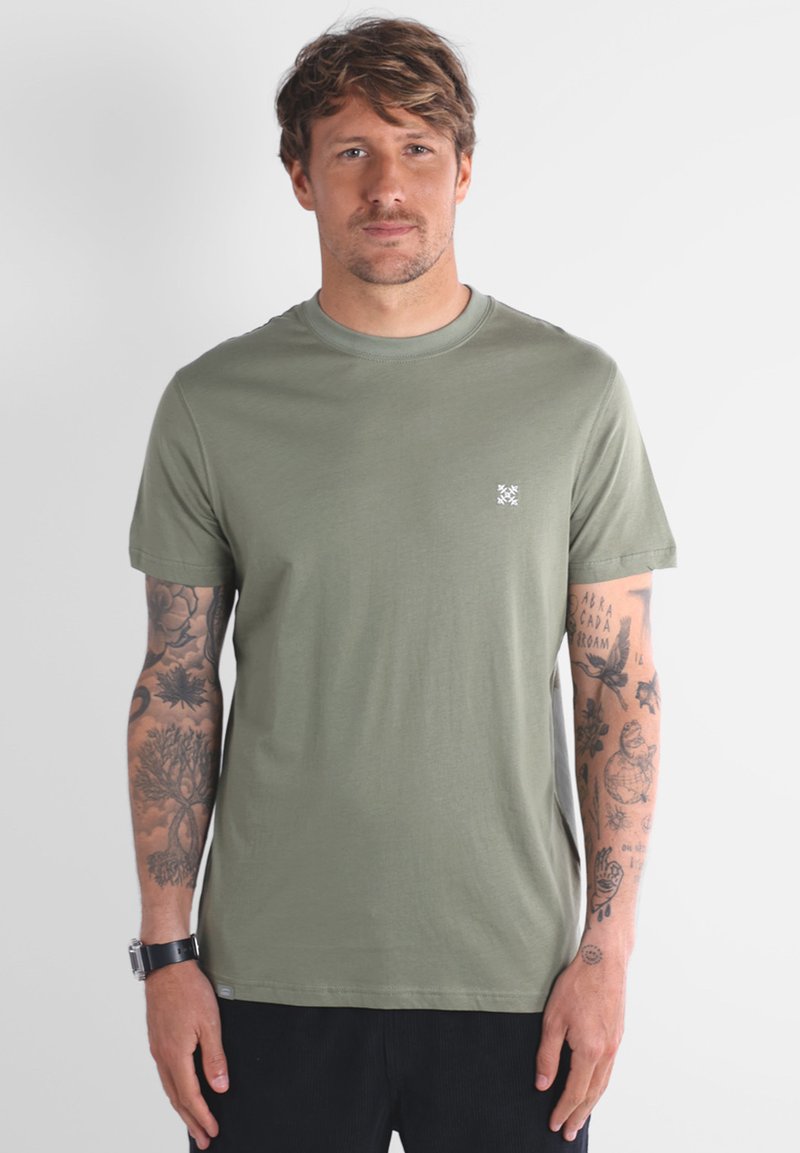 T-shirt vert olive en coton, avec un col rond et des manches courtes. Petit logo blanc sur la poitrine. Texture lisse.