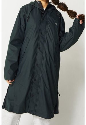 Impermeable largo con capucha de color verde oscuro, con botones en la parte delantera y bolsillos laterales, usado por una persona que sostiene una coleta trenzada.