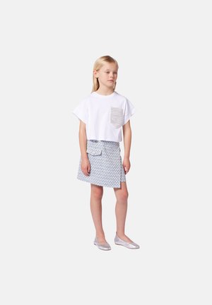 T-shirt blanc court avec une poche texturée, associé à une jupe à rayures en zigzag bleu et blanc et des ballerines argentées.