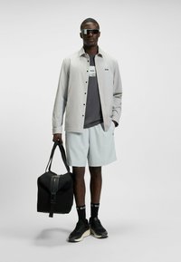 Light gray button-up shirt, dark gray t-shirt, mint green shorts, black sneakers, oversized black bag, dark sunglasses.