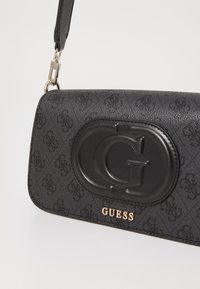 Schwarze, strukturierte, synthetische Handtasche mit glänzendem Logo-Akzent und goldfarbener Markenbeschriftung, ausgestattet mit einem abnehmbaren Schultergurt.