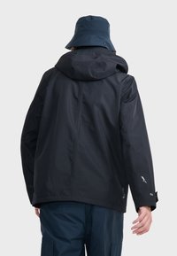 Veste imperméable bleu marine foncé avec capuche, à la texture lisse et aux poignets ajustables. Associée à un chapeau seau assorti.