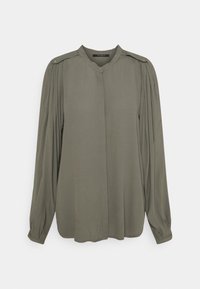 Långärmad blus i olivgrön med plisserade axlar, dold knappslå och knäppte ärmslut på en enfärgad bakgrund.