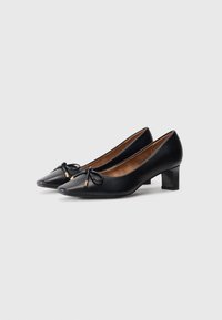 Black leather high-heeled shoes with a pointed toe, decorative bow detail, and a medium block heel. Smooth texture overall.