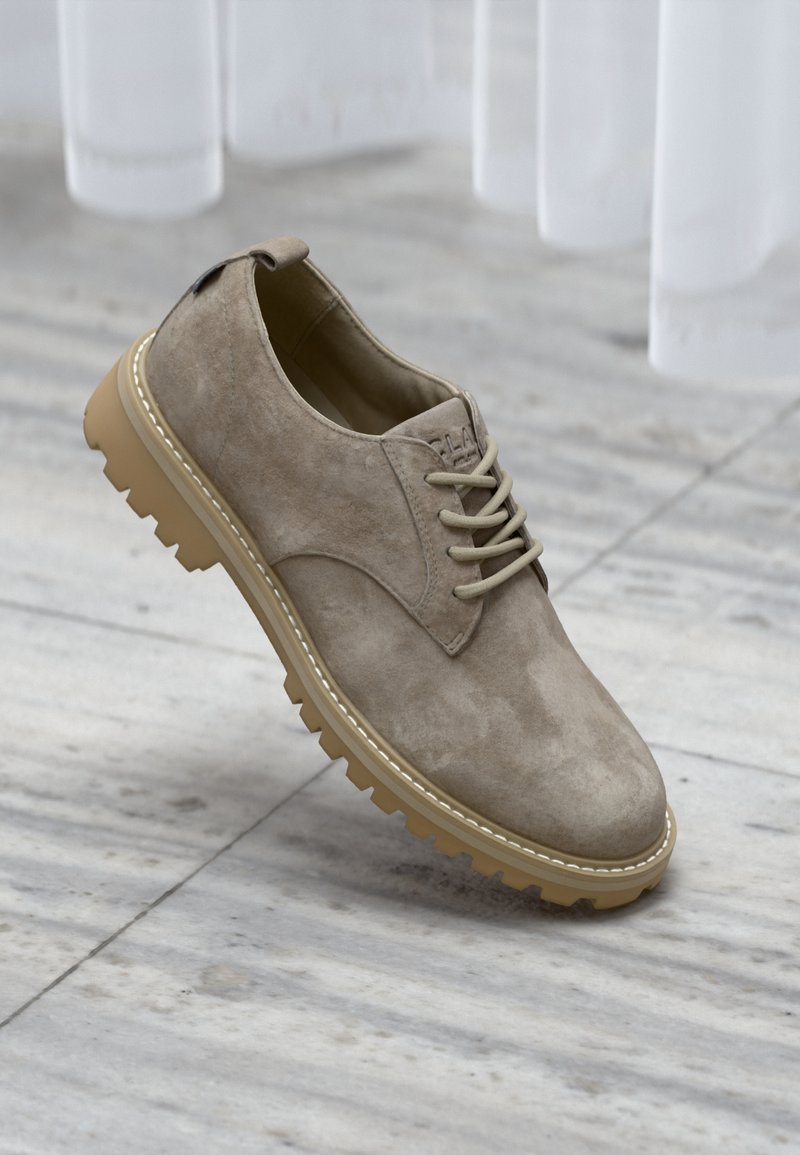 Μπεζ μοκασίνι από σουέντ με χοντρή καφέ λαστιχένια σόλα σε μαρμάρινο δάπεδο, τοποθετημένο κοντά σε λευκές κουρτίνες.