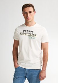 Camiseta de algodón blanca con gráfico de "PETROL INDUSTRIES & CO" en verde oscuro y negro. Manga corta, cuello redondo, diseño ajustado.
