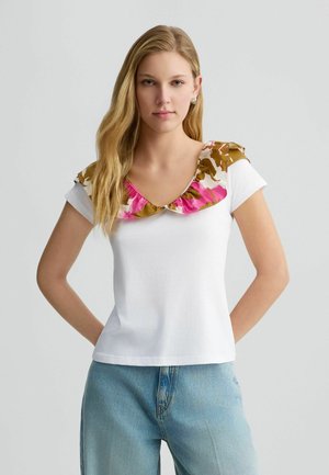 T-shirt blanc à manches courtes, doté d'un col à volants fleuri aux teintes rose, marron et crème. Tissu en coton doux, coupe décontractée.