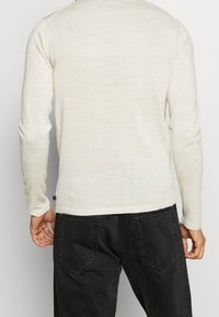 Ljusbeige långärmad tröja med slät textur och ribbade muddar, kombinerad med svarta denimjeans med bakfickor.