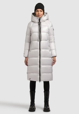 Padded long coat in light gray with a hood, front zipper, and black accents. Styled with black leggings and lace-up boots.