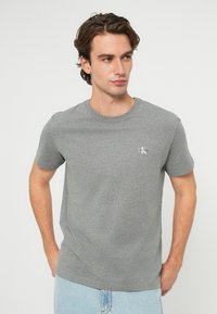 Szürke pamut póló kerek nyakkal, rövid ujjakkal és egy kis fehér logóval a bal mellrészen. Egyszerű kialakítás, puha anyag.