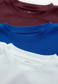 Trzy t-shirty z okrągłym dekoltem ułożone jeden na drugim: burgundowy, niebieski i biały. Miękka tkanina z detalami w postaci ściągacza przy dekolcie. Minimalistyczny design w jednolitych kolorach.