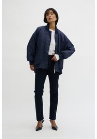 Navy bomber jacket with a smooth finish, zip closure, and ribbed cuffs; paired with dark straight-leg jeans and black pointed heels.