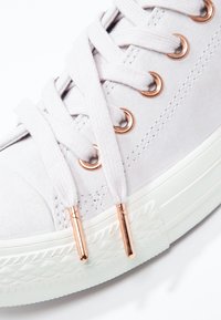 Baskets en daim gris clair avec semelle en caoutchouc blanc, œillets et embouts en or rose, et lacets blancs plats en motif croisé.