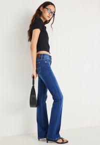 Niebieskie dzwony z ciemnym wybarwieniem, zestawione z dopasowanym czarnym topem. Dodatki to mała czarna torebka i czarne sandały na paski.