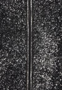 Czarna teksturowana tkanina z zamkiem błyskawicznym pośrodku, posiadająca wypukłą, kamienistą powierzchnię dla zwiększenia wymiaru i wizualnego zainteresowania.