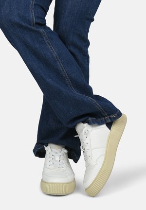 Witte sneakers van gewatteerd leer met lichte rubberen zolen, gecombineerd met donkerblauwe spijkerbroeken met zichtbare stiksel en een lichte flare.