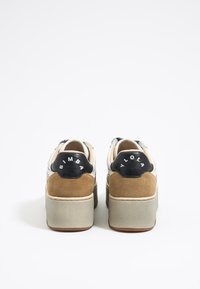 Zapatillas de plataforma que presentan una mezcla de texturas, incluyendo cuero negro, ante y tela crema, con acentos en el talón en contraste y branding en relieve.