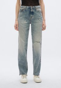 Dżinsy z denimu w jasnoniebieskim kolorze z efektami postarzenia, z przetarciami, luźnym krojem i surowymi krawędziami nogawek. Uzupełnione białymi trampkami.